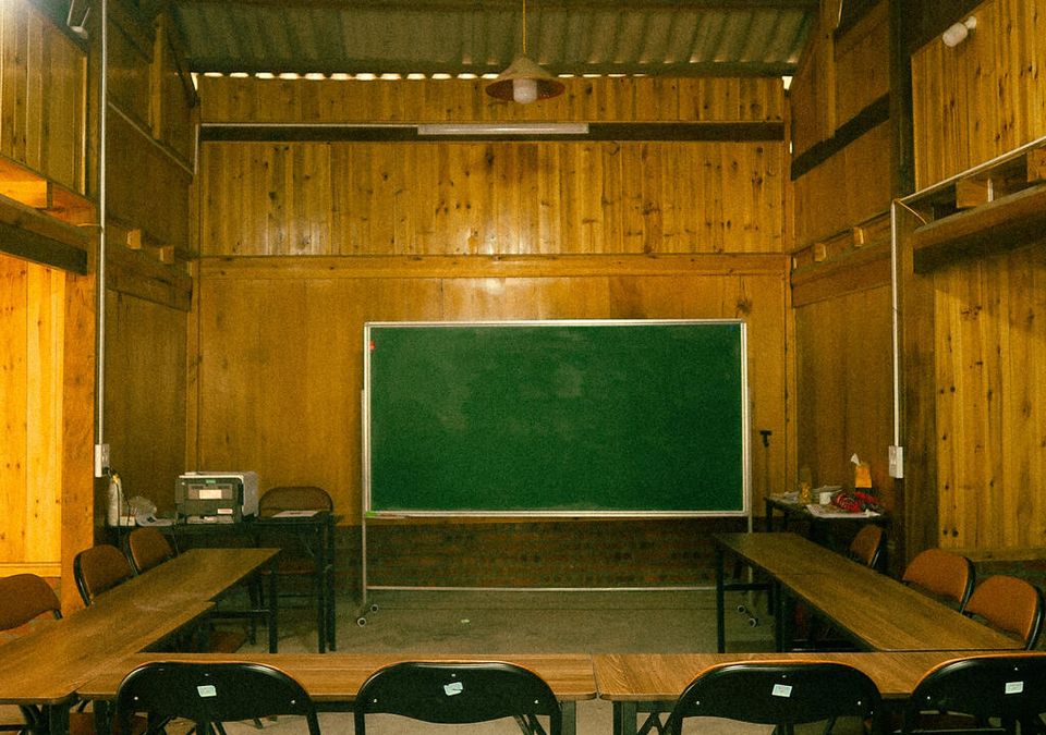 La salle de classe vide avant le cours : des murs en pin chaleureux, un tableau vert, des pupitres disposés en U.