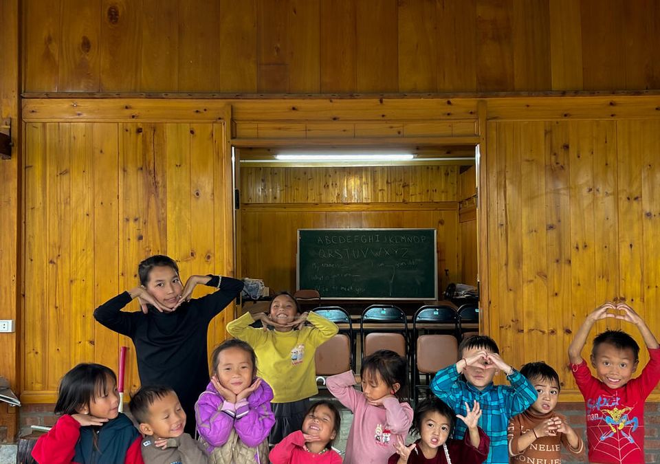 Une douzaine d'enfants faisant des cœurs avec les mains et des grimaces devant le tableau de l'alphabet.