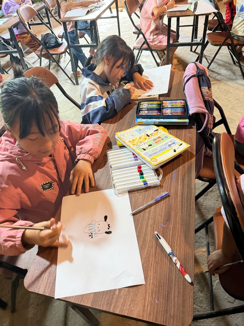 Deux fillettes dessinant aux crayons et aux feutres à un pupitre de la classe.