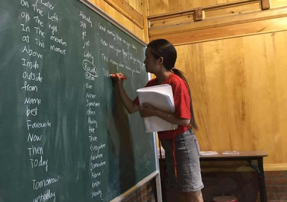 Un élève en tee-shirt rouge écrivant du vocabulaire anglais au tableau vert.