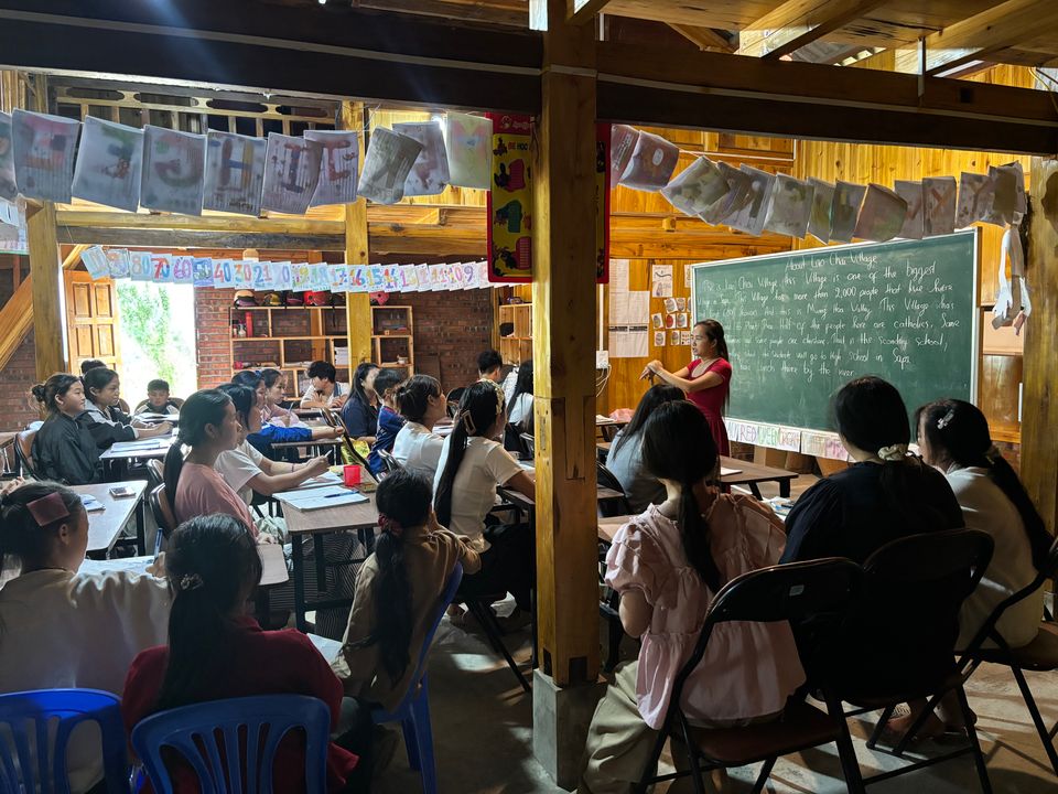 Miss Ha enseignant au tableau, vue depuis une salle pleine d'élèves.