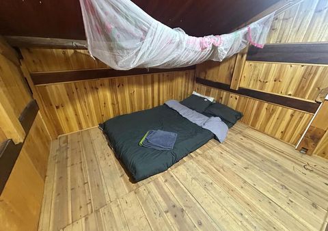 Une chambre sous les combles avec un matelas fait, des serviettes pliées et une moustiquaire sous les poutres en bois.