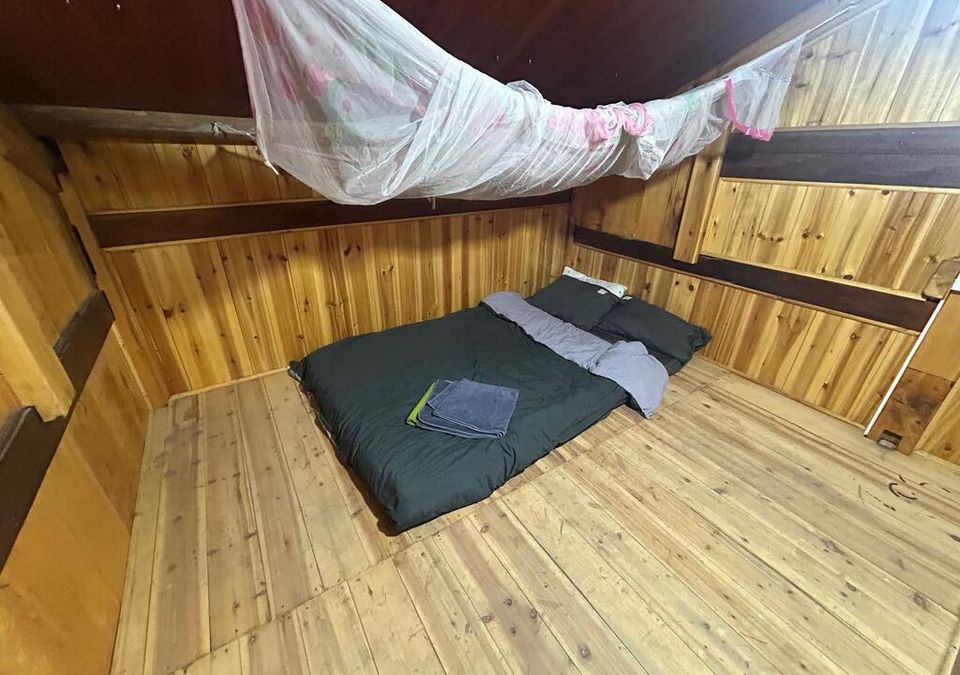An attic room with a made-up mattress, folded towels, and a mosquito net under timber beams.