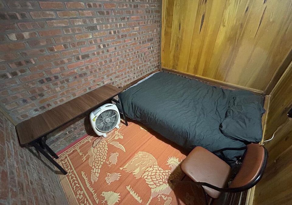 A private room with a double bed, brick and timber walls, a desk and a patterned rug.