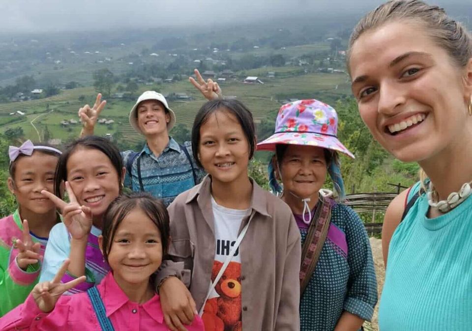 Le selfie d'un bénévole sur un sentier brumeux avec des enfants souriants et une grand-mère hmong au chapeau fleuri.