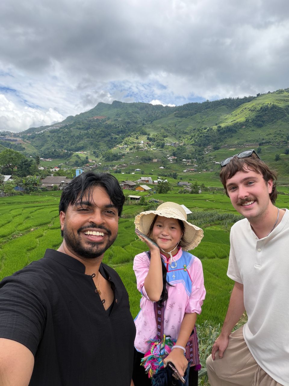 Deux voyageurs et une jeune guide en tenue traditionnelle au-dessus des rizières en terrasses verdoyantes de la vallée.